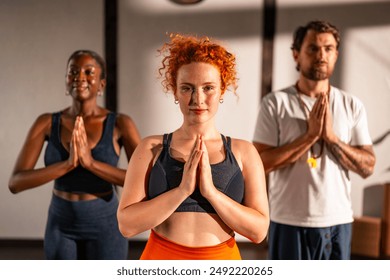 A diverse group of people practicing yoga indoors, hands in prayer position, selective focus. - Powered by Shutterstock