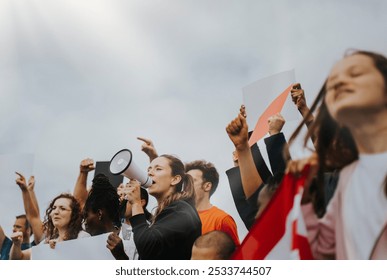 Diverse group of people at a protest, holding signs and raising fists. Protesters, signs, and fists. Unity and activism. Diverse men and women protest outdoor against the sky. Woman holding megaphone - Powered by Shutterstock