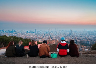 A diverse group of people sits on the edge of the Bunkers del Carmel, a popular viewpoint in Barcelona, Spain, as they take in the breathtaking panoramic view of the city at sunset.  - Powered by Shutterstock