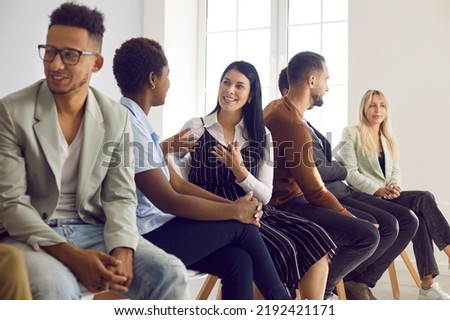 Diverse group of people speaking English at language learning center. Multi ethnic adult students sitting on row of chairs, talking to each other, discussing ideas, and practicing communicative