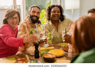 Diverse group of people in their 40s enjoying lunch together, smiling and toasting over italian, spanish, and mediterranean dishes at a casual home gathering - Powered by Shutterstock