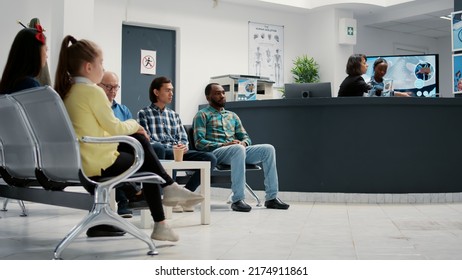 Diverse group of people waiting in hospital reception lobby to attend medical appointment with general practitioner. Patients in waiting room lobby sitting at healthcare clinic. Tripod shot.