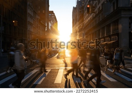 Diverse group of people walking across the crowded intersection at 23rd Street and 5th Avenue in New York City with bright light of sunshine in the background
