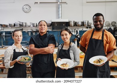 Diverse group of people wearing aprons and holding gourmet dishes in professional kitchen - Powered by Shutterstock