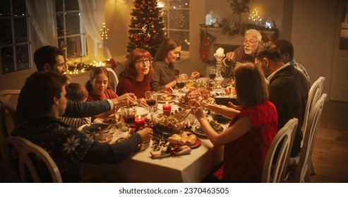 Diverse Group of People, Young and Old, Share a Joyful Christmas Dinner at Home. Family Sitting Behind a Big Dining Table Full of Delicious Food with Roast Turkey Feast. High Angle Evening - Powered by Shutterstock