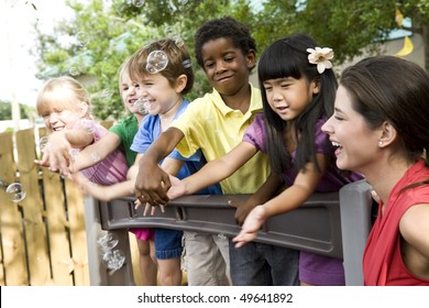 Diverse Group Of Preschool 5 Year Old Children Playing In Daycare With Teacher