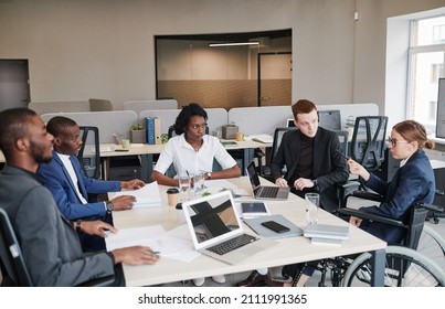 Diverse Group Of Professional Business People At Meeting Table In Office With Woman Using Wheelchair