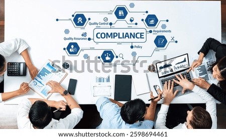 A diverse group of professionals in a collaborative workspace discussing compliance strategy and analyzing quality control reports using modern technology and data visualization tools. Amity