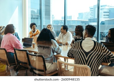 A diverse group of professionals engaged in a collaborative meeting in a modern city office. The urban skyline provides a scenic backdrop as the team discusses strategies, fostering corporate synergy.