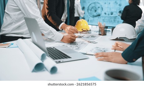 A diverse group of professionals engaged in collaborative planning over construction documents in a modern office setting. Tools and technology enhance productivity. SACTR