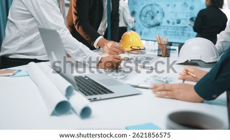 A diverse group of professionals engaged in collaborative planning over construction documents in a modern office setting. Tools and technology enhance productivity. SACTR