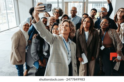 A diverse group of professionals taking a cheerful selfie together during a seminar or workshop. They are smiling and appear engaged. - Powered by Shutterstock