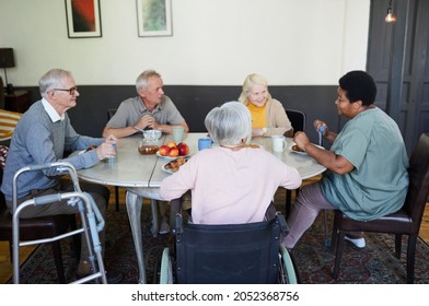 Diverse Group Of Senior People Chatting At Dinner Table In Nursing Home