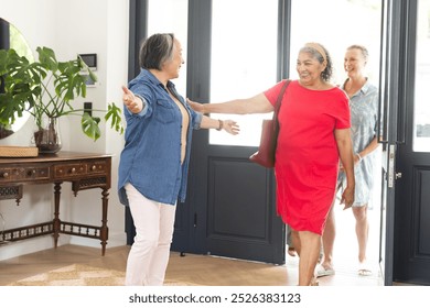 Diverse group of senior women greeting each other with open arms and smiles. Bright, welcoming home entrance with natural light streaming through large windows, unaltered - Powered by Shutterstock