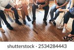 Diverse group sitting in a circle, engaged in discussion, wooden floor. Focus on hands and legs, showing interaction and communication. Diverse people sitting in a circle of support from community.