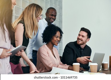 Diverse Group Of Smiling Business Colleagues Talking And Working Together On A Laptop At A Desk In A Modern Office