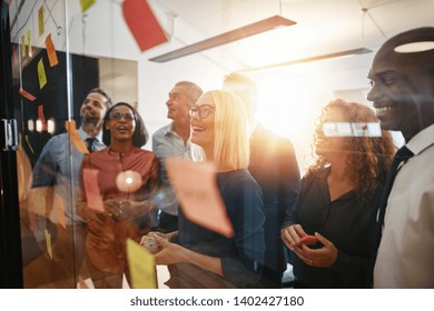 Diverse group of smiling businesspeople brainstorming together with sticky notes on a glass wall while working in a modern office - Powered by Shutterstock