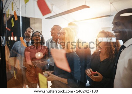 Diverse group of smiling businesspeople brainstorming together with sticky notes on a glass wall while working in a modern office