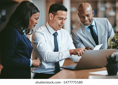 Diverse group of smiling businesspeople reading paperwork together while working on a laptop at a table in an office - Shutterstock ID 1477775180