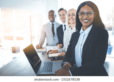 Diverse group of smiling businesspeople standing in a row at a table during a meeting together in a bright modern office