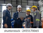 A diverse group of smiling industrial professionals collaborates over a laptop on the factory floor, embodying teamwork and technological integration in manufacturing.