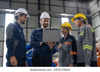 A diverse group of smiling industrial professionals collaborates over a laptop on the factory floor, embodying teamwork and technological integration in manufacturing. - Powered by Shutterstock