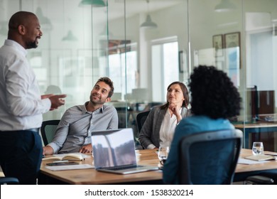Diverse group of smiling staff listening to their manager during a meeting together around a table in a modern office - Shutterstock ID 1538320214