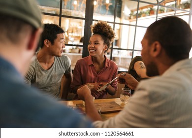 Diverse group of smiling young friends sitting at a table in a bistro talking together over a meal