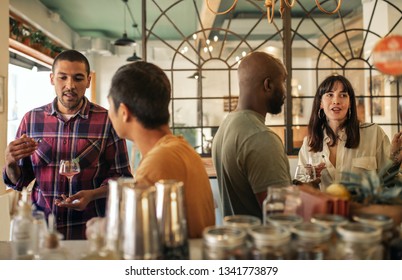 Diverse group of smiling young friends sitting together at a table in a trendy bar having drinks and talking together