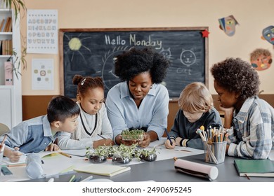 Diverse group of students and female teacher over table looking at microgreen sprouts studying growth of plants and learning about environment in classroom - Powered by Shutterstock