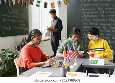 Diverse group of students sitting at table during lesson in school classroom and using gadgets, copy space