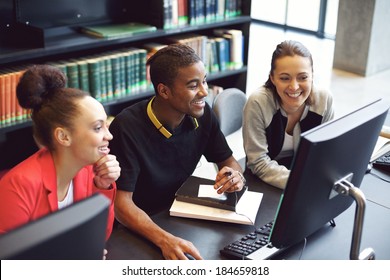 Diverse group of students using computer for finding information for their academic project. Happy young people sitting at table with books and computer taking notes for their study.