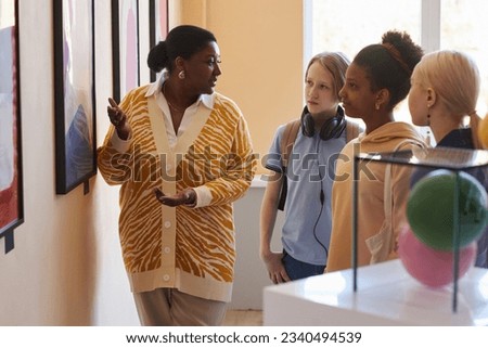 Diverse group of teenagers listening to black woman explaining modern art in museum