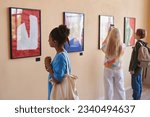 Diverse group of teenagers looking at abstract art in art gallery or museum standing in row with African American girl in foreground