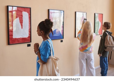 Diverse group of teenagers looking at abstract art in art gallery or museum standing in row with African American girl in foreground