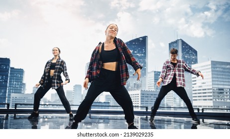 Diverse Group Of Three Professional Dancers Performing A Hip Hop Dance Routine In Front Of A Big Digital Led Wall Screen With Modern Urban Skyline With Office Skyscrapers In Studio Environment.