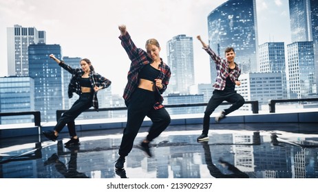 Diverse Group Of Three Professional Dancers Performing A Hip Hop Dance Routine In Front Of A Big Digital Led Wall Screen With Modern City Skyline With Office Skyscrapers In Studio Environment.