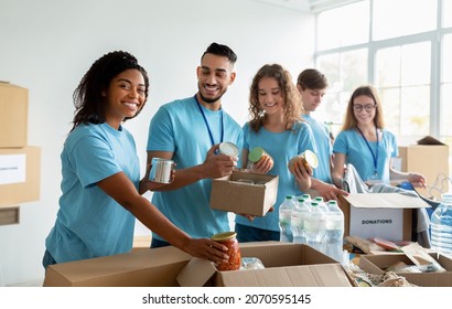 Diverse group of volunteers sorting donated food in boxes, working in community charity donation center and smiling at camera, preparing boxes for poor and homeless people - Powered by Shutterstock