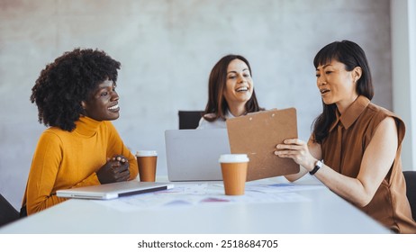 A diverse group of women engage in a collaborative business meeting in a modern office setting, fostering teamwork and creativity. - Powered by Shutterstock