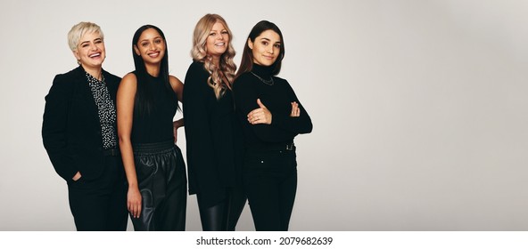 Diverse Group Of Women Smiling In A Studio. Four Happy Women Looking At The Camera While Standing Together Against A Studio Background. Group Of Fashionable Women Standing In A Studio.