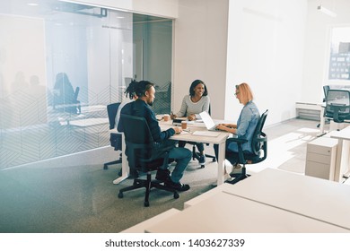 Diverse Group Of Work Colleagues Laughing Together During A Meeting Around A Table Inside Of An Office