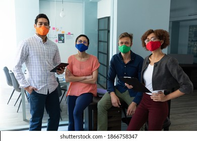 Diverse Group Of Work Colleagues Wearing Masks In An Office. Standing And Talking Together, One Man Holding A Tablet Computer. Hygiene In Workplace During Coronavirus Covid 19 Pandemic.