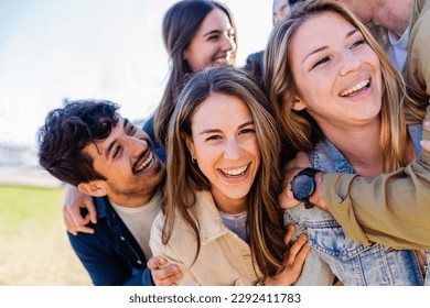 Diverse group of young adult friends having fun hugging each other outside. Joyful millennial people laughing enjoying time together. Community and friendship concept - Powered by Shutterstock