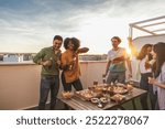 Diverse group of young adults having fun with drinks and pizza at a sunset rooftop gathering.