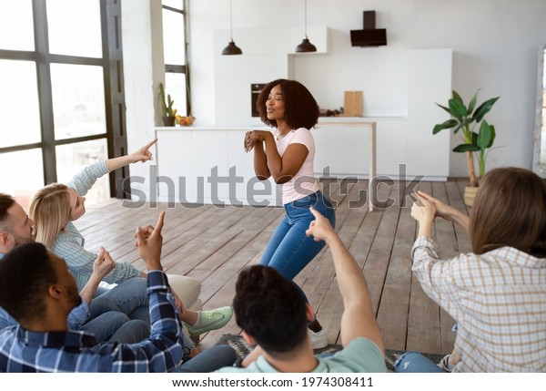 Diverse group of young best friends playing\
charades in living room, trying to guess word on student party.\
Millennial youth entertaining themselves with guessing game,\
spending fun time\
together