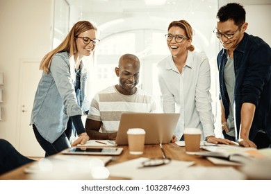 Diverse group of young businesspeople laughing while working together over a laptop at a table in an office