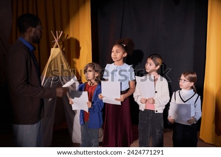 Diverse group of young children actors listening to drama teacher rehearsing school play on stage in theater