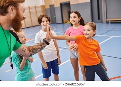 A diverse group of young children enthusiastically stand around each other in a gym setting while listening to their male teachers instructions. - Powered by Shutterstock