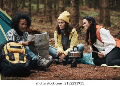 Diverse Group Of Young Female Friends Sitting At Their Forest Campsite Making Coffee And Reading A Trail Map