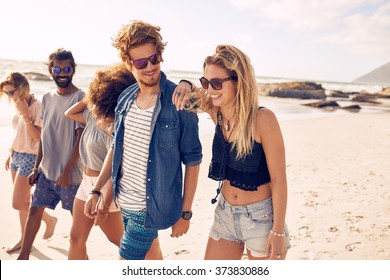 Diverse group of young friends having a walk on the beach. Young people looking happy on vacation. Young men and woman walking on coast.